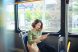Beautiful happy young woman sitting in city bus, looking at mobile phone